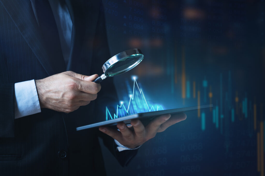 Homem de terno com lupa e tablet exibindo gráficos digitais, representando gestão financeira inteligente com análise de dados.